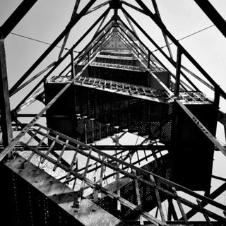 Black and white picture of a metal tower with stairs - by Alex Ogg